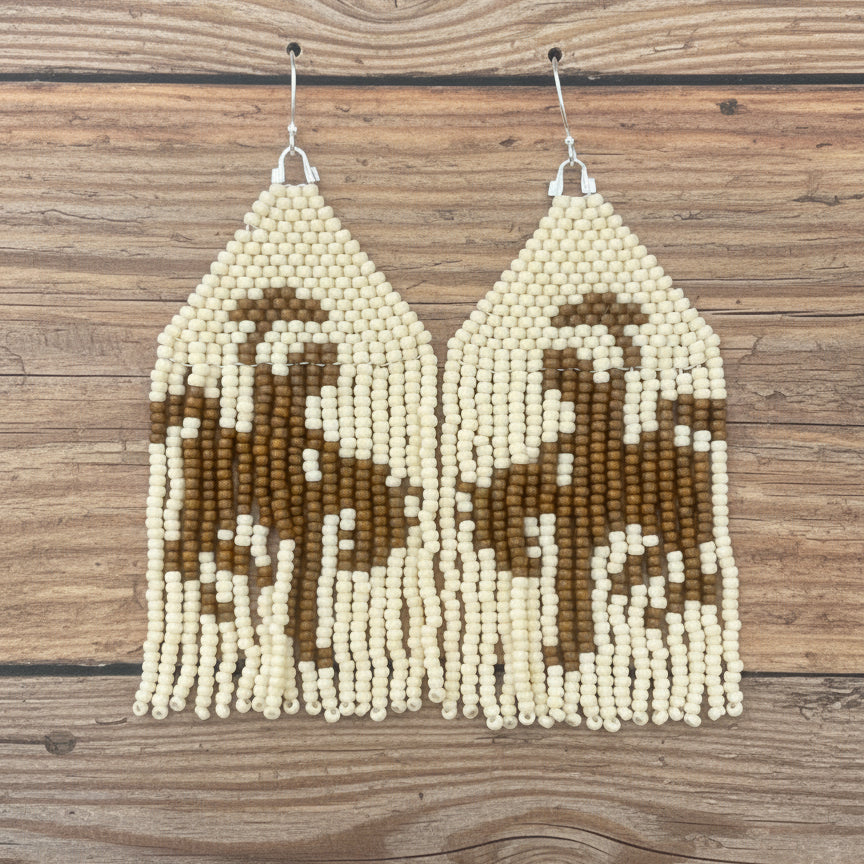 A pair of brown and beige beaded fringe earrings depicting a cowboy on a horse, displayed on a card with 'Badlands Beadwork' written at the top.