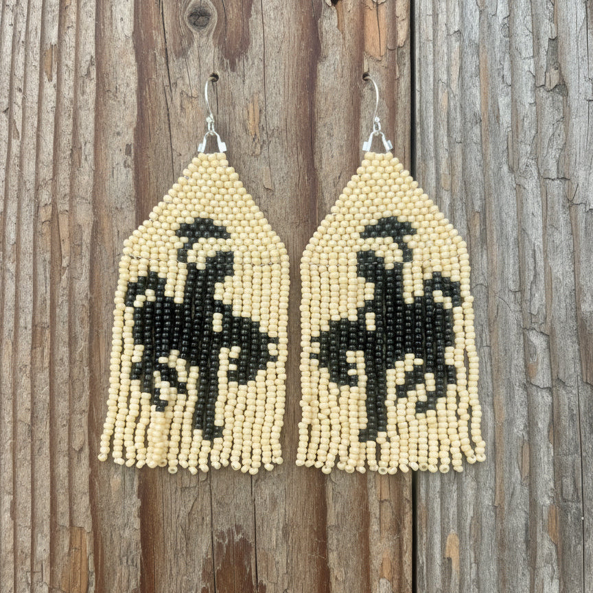 A pair of beaded fringe earrings depicting a black and cream cowboy on horse design, displayed against a white background with 'Badlands Beadwork' written at the top.