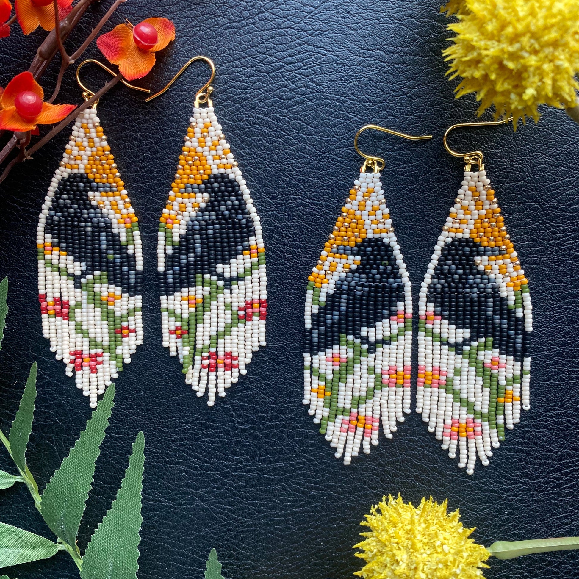 Pair of beaded Raven earrings on a dark textured surface with flowers and leaves.