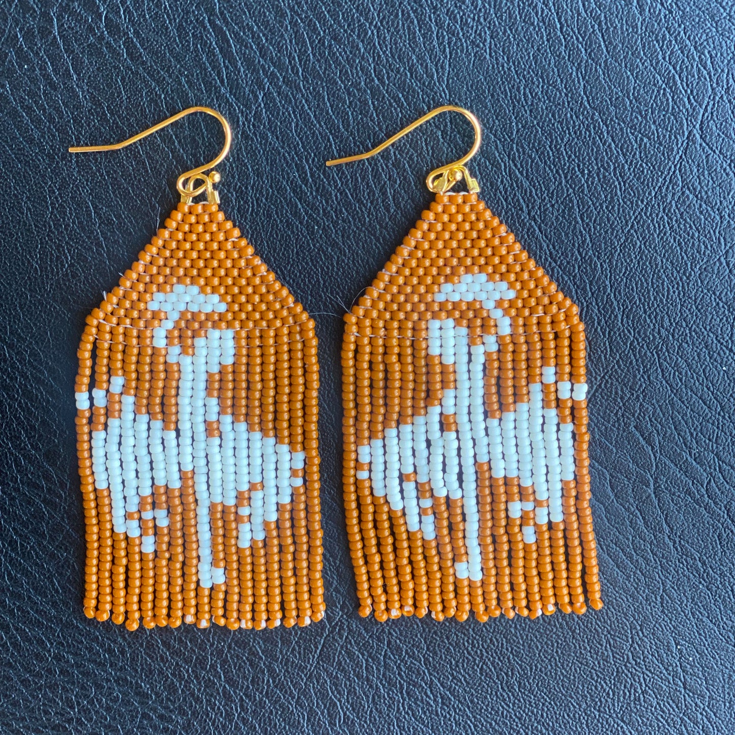 A pair of rust brown and white beaded fringe earrings designed to resemble a cowboy on a bucking horse.